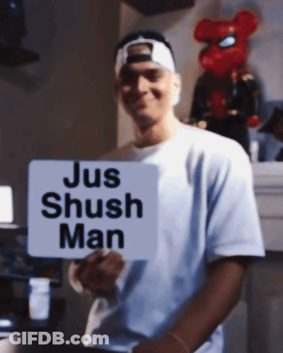 A Man In A White Shirt Holds A Sign That Says Jus Shush Man GIF