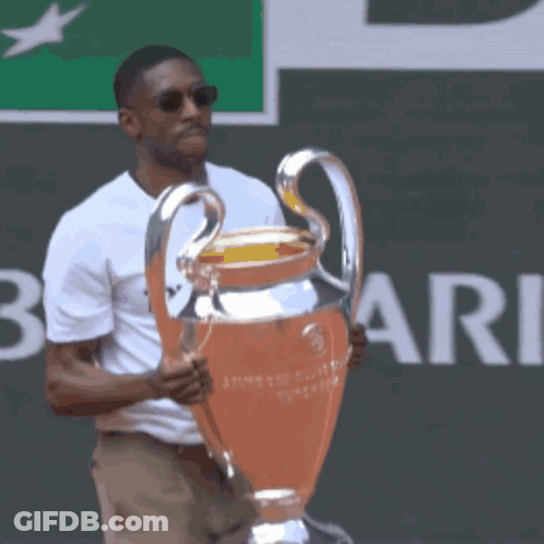 A Man In A White Shirt Holds A Trophy In Front Of A Sign That Says Rie GIF