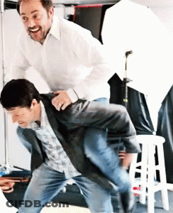 A Man In A White Shirt Is Carrying Another Man On His Shoulders GIF