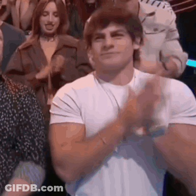 A Man In A White Shirt Is Clapping His Hands In Front Of A Crowd Of People . GIF