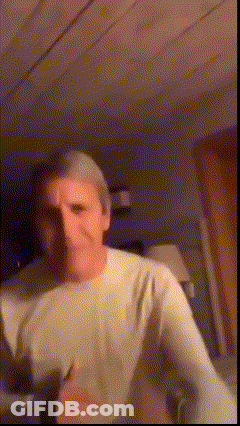 A Man In A White Shirt Is Dancing In A Dark Room . GIF