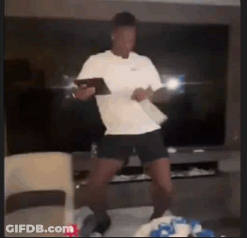 A Man In A White Shirt Is Dancing In A Living Room While Holding A Tablet . GIF