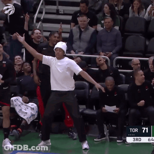 A Man In A White Shirt Is Dancing In Front Of A Crowd At A Sports Game GIF