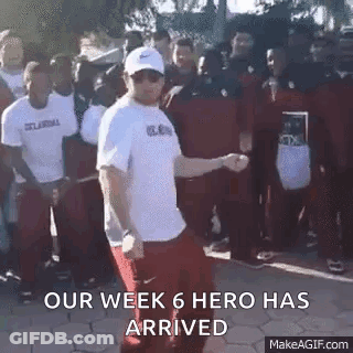 A Man In A White Shirt Is Dancing In Front Of A Crowd Of People With The Words `` Our Week 6 Hero Has Arrived '' . GIF