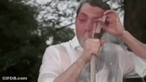 A Man In A White Shirt Is Drinking From A Straw . GIF