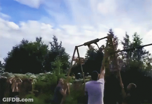 A Man In A White Shirt Is Hanging From A Rope In Front Of A Crowd Of People GIF