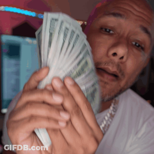 A Man In A White Shirt Is Holding A Bunch Of Money In Front Of His Face GIF