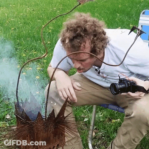 A Man In A White Shirt Is Holding A Camera And Looking At Something GIF