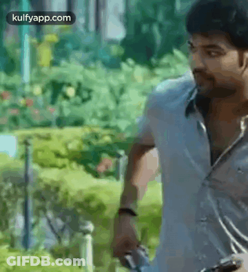 A Man In A White Shirt Is Holding A Gun In His Hand . GIF