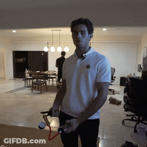 A Man In A White Shirt Is Holding A Hose In His Hand GIF