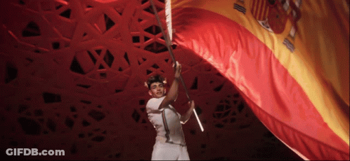 A Man In A White Shirt Is Holding A Large Red And Gold Flag GIF