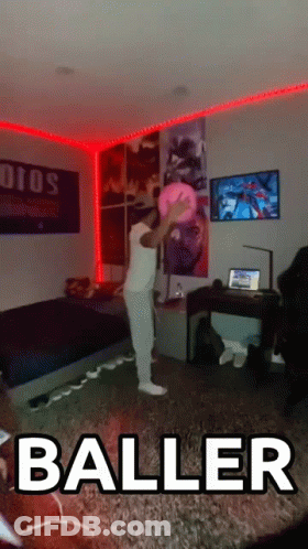 A Man In A White Shirt Is Holding A Pink Ball In A Living Room With The Word Baller On The Floor GIF