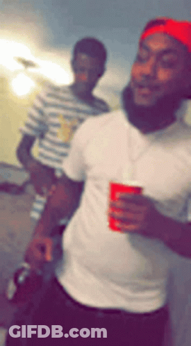 A Man In A White Shirt Is Holding A Red Cup And Smiling GIF