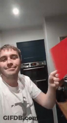 A Man In A White Shirt Is Holding A Red Piece Of Paper In His Hand . GIF