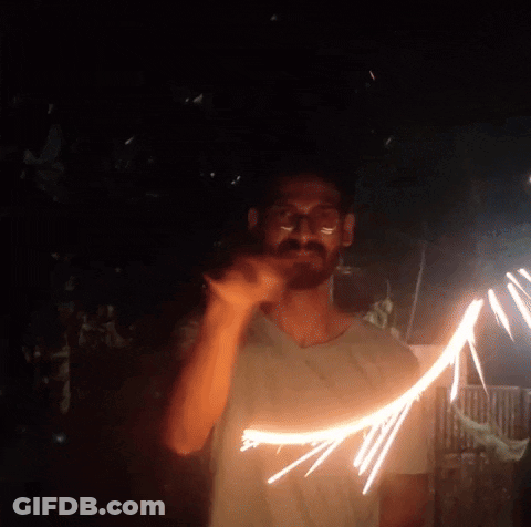 A Man In A White Shirt Is Holding A Sparkler In The Dark GIF