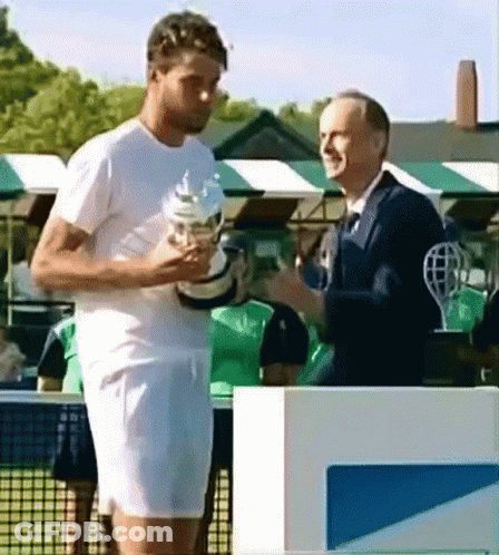 A Man In A White Shirt Is Holding A Trophy And Talking To Another Man In A Suit GIF