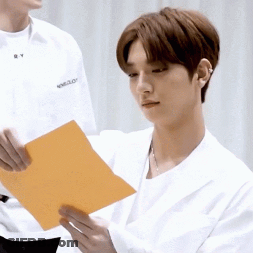 A Man In A White Shirt Is Holding An Orange Piece Of Paper In His Hands . GIF