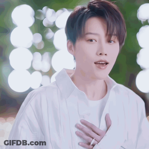A Man In A White Shirt Is Holding His Hands To His Chest GIF