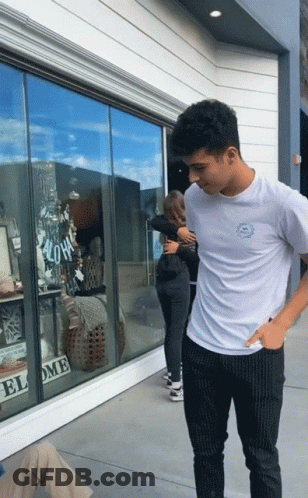 A Man In A White Shirt Is Hugging A Woman In Front Of A Store Window That Says " Aloha " GIF