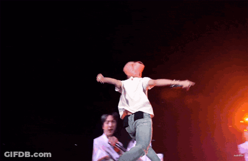 A Man In A White Shirt Is Jumping In The Air On A Stage GIF