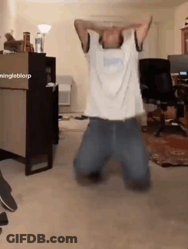 A Man In A White Shirt Is Kneeling Down In A Living Room With His Hands On His Head . GIF