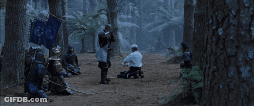 A Man In A White Shirt Is Kneeling Down Next To A Man In Armor With A Sword GIF