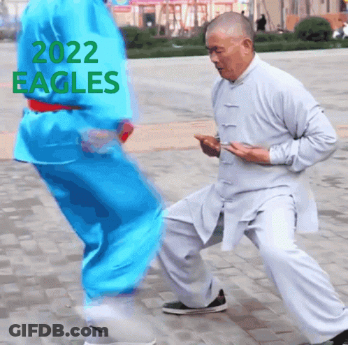 A Man In A White Shirt Is Kneeling Down Next To Another Man In A Blue Shirt With 2022 Eagles Written On The Top GIF