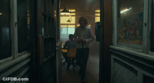 A Man In A White Shirt Is Laughing While Standing In Front Of A Window GIF
