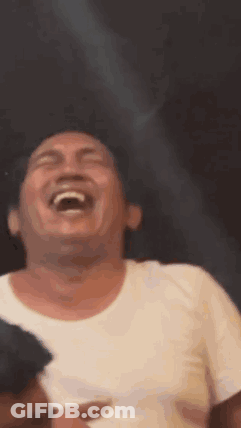 A Man In A White Shirt Is Laughing With His Mouth Open And His Eyes Closed . GIF