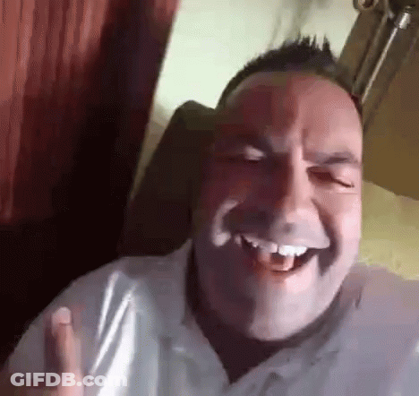 A Man In A White Shirt Is Laughing With His Mouth Open While Sitting In A Chair . GIF