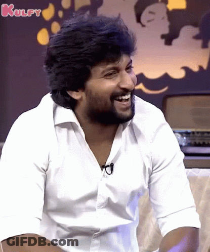 A Man In A White Shirt Is Laughing With The Word Kulfy In The Background GIF
