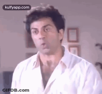 A Man In A White Shirt Is Making A Funny Face And Looking At The Camera . GIF