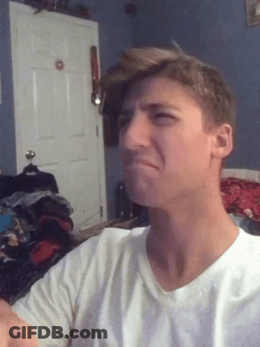 A Man In A White Shirt Is Making A Funny Face In Front Of A Door GIF