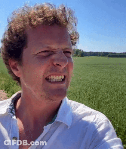 A Man In A White Shirt Is Making A Funny Face In Front Of A Green Field GIF