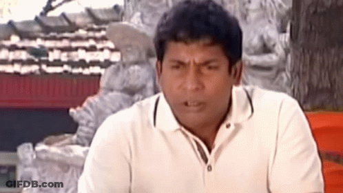 A Man In A White Shirt Is Making A Funny Face While Sitting In Front Of A Statue . GIF