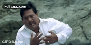 A Man In A White Shirt Is Making A Funny Face While Sitting On A Rock . GIF
