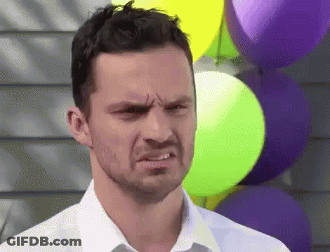 A Man In A White Shirt Is Making A Funny Face While Standing In Front Of Balloons . GIF