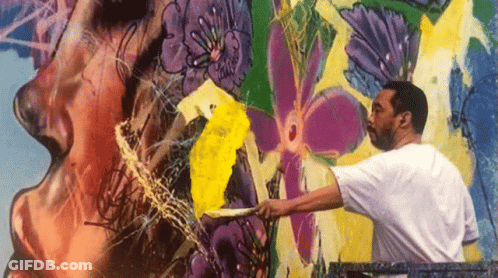 A Man In A White Shirt Is Painting A Colorful Mural On A Wall GIF