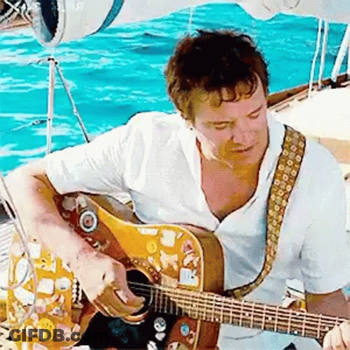 A Man In A White Shirt Is Playing A Guitar On A Boat . GIF