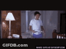 A Man In A White Shirt Is Playing A Video Game In A Dark Room . GIF