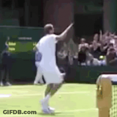 A Man In A White Shirt Is Playing Tennis On A Green Court GIF