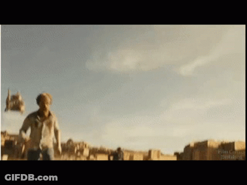 A Man In A White Shirt Is Running In A Field With A Blue Sky Behind Him GIF