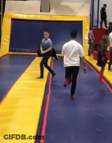A Man In A White Shirt Is Running On A Trampoline While A Boy In A Blue Shirt Watches GIF