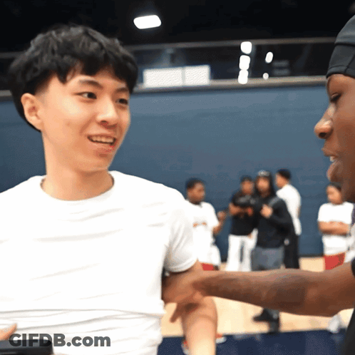 A Man In A White Shirt Is Shaking Hands With Another Man In A Black Hat GIF