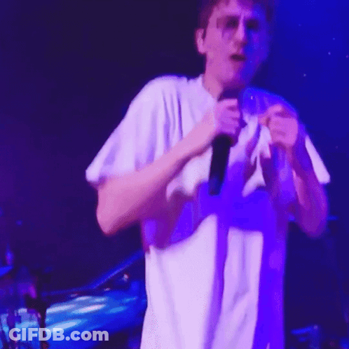 A Man In A White Shirt Is Singing Into A Microphone On Stage GIF