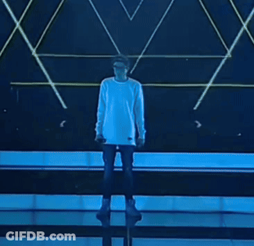 A Man In A White Shirt Is Singing Into A Microphone On Stage GIF