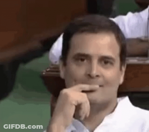 A Man In A White Shirt Is Sitting At A Table With His Hand To His Chin . GIF