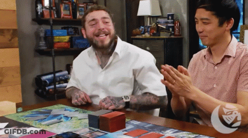 A Man In A White Shirt Is Sitting At A Table With Two Other Men Applauding GIF