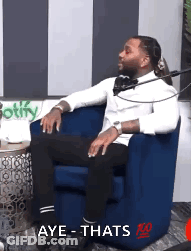 A Man In A White Shirt Is Sitting In A Blue Chair With The Words Aye Thats 100 On The Chair GIF
