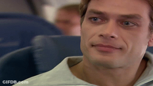 A Man In A White Shirt Is Sitting In A Blue Seat On An Airplane GIF